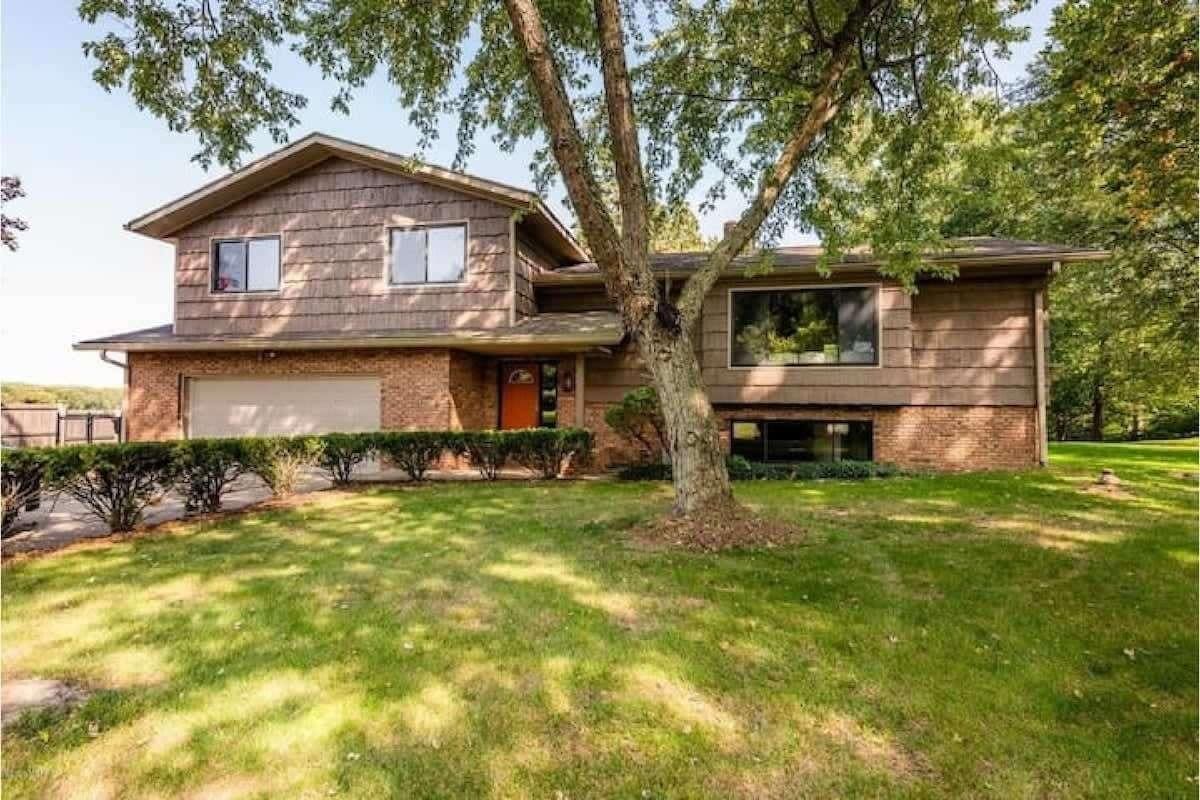Spacious vacation rental home with brick and wood exterior, large front yard, and mature trees near 