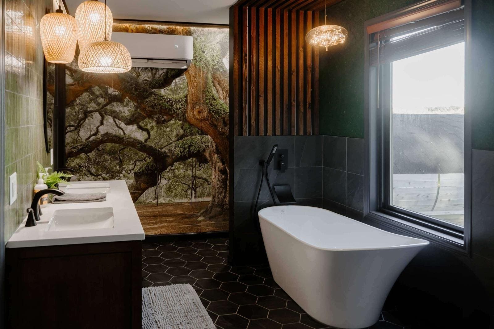 Modern bathroom with freestanding tub, forest mural, pendant lights, and dark tile floor in a nature